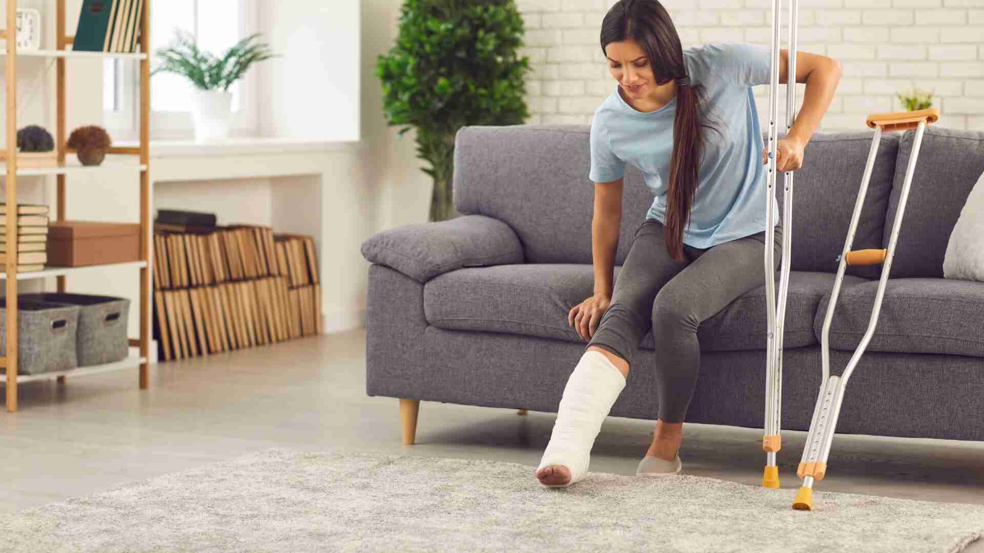 Frau sitzt auf einem Sofa mit einem Gipsverband am Bein und Krücken neben sich.